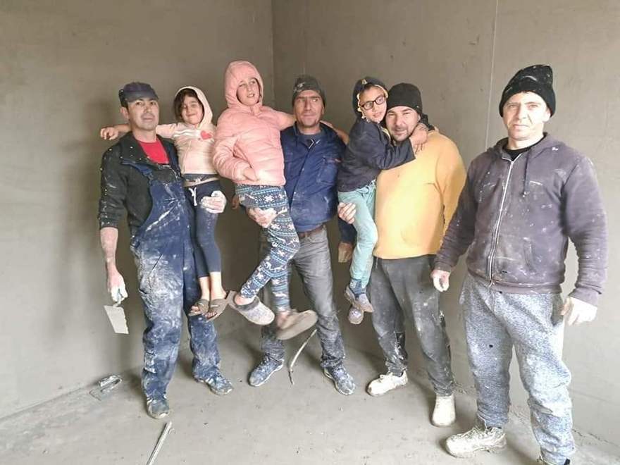 Muncitorii voluntari ținând în brațe copiii familiei Manea, în camera proaspăt tencuită