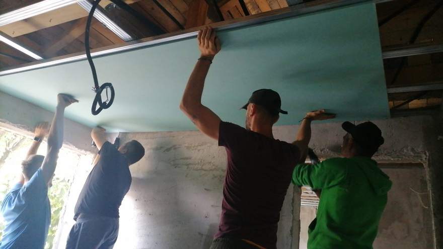 Echipa de voluntari ridicând o placă de rigips pe tavan